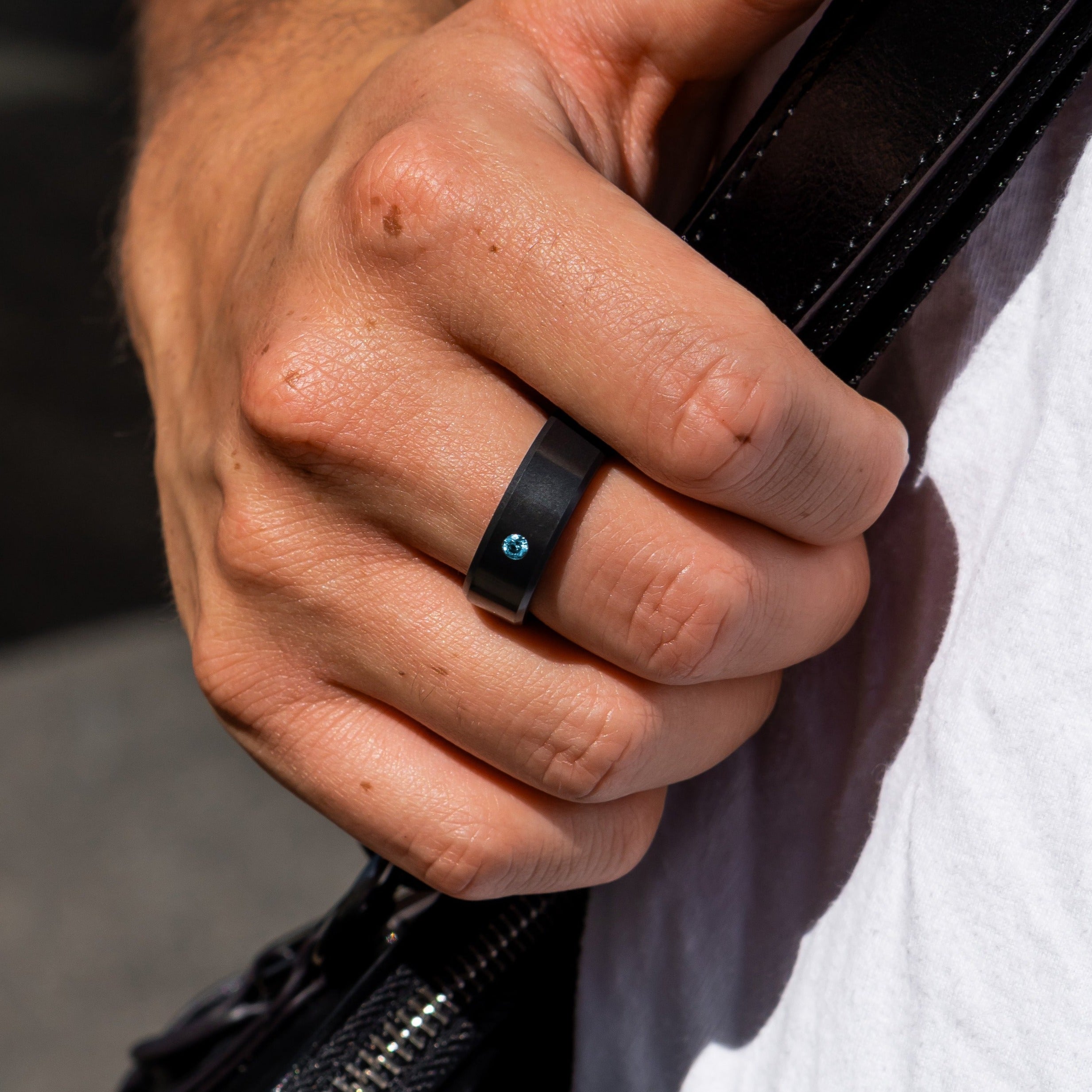 Lifestyle shot #1 of men's hands wearing our Elysium ARES Men's Black Diamond & Blue Diamond Inset | ElysiumBlack.com | Men’s Blue Diamond Wedding Rings