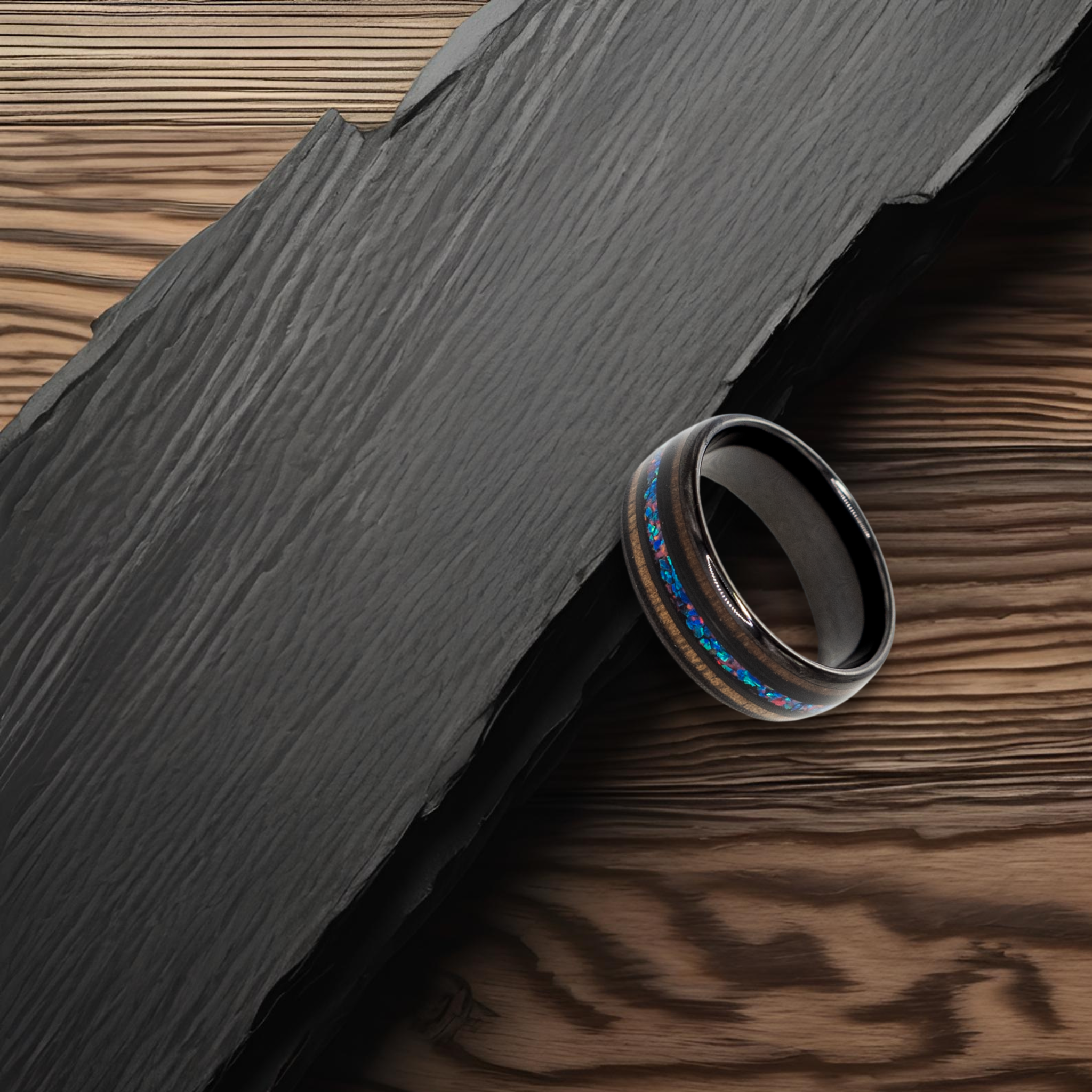 Nereus ring – Black Tungsten featuring Double Koa Wood and Crushed Opal Inlays from the Hustler Collection. Lifestyle shot, placed on textured rock.