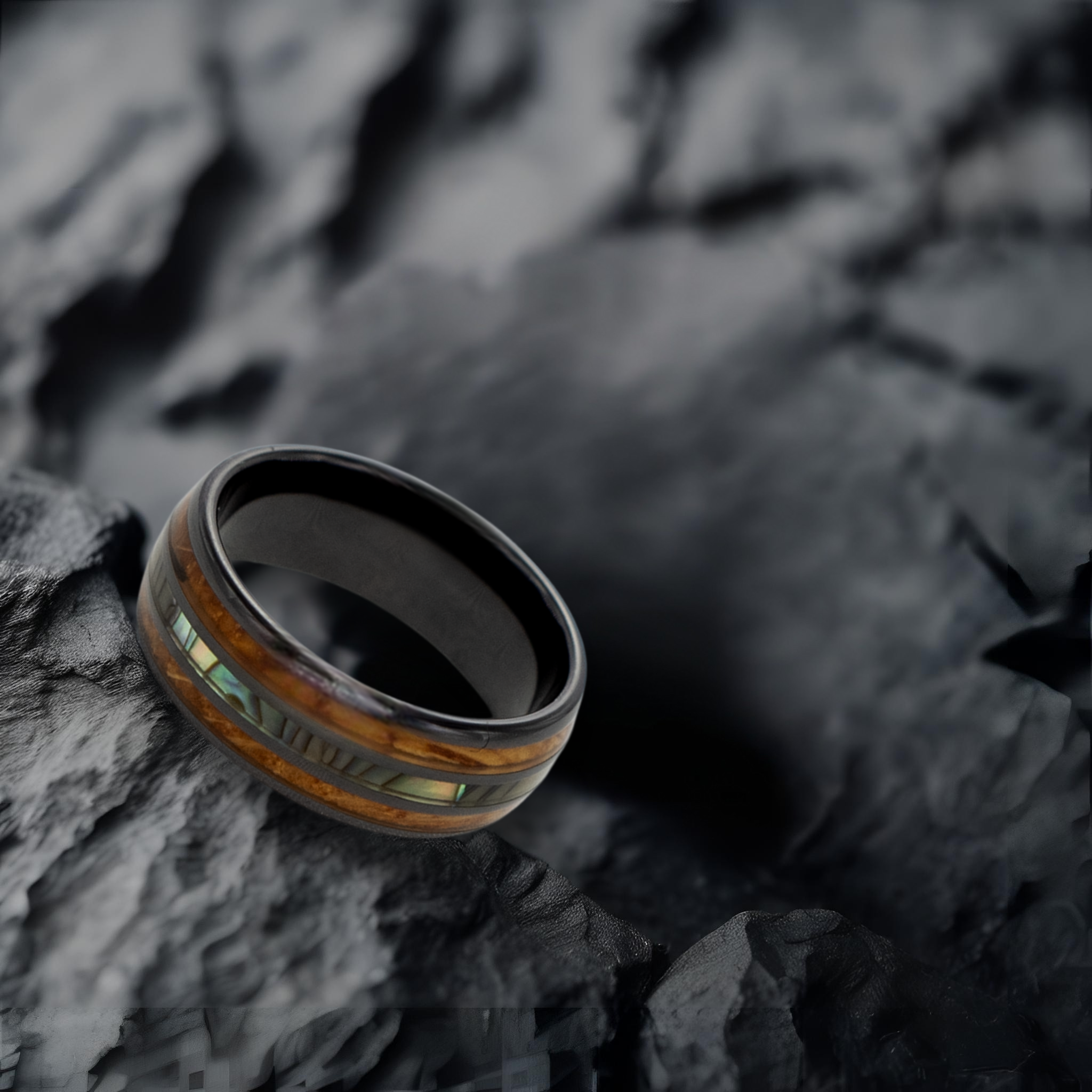 Odysseus ring – Polished Black Ceramic, Featuring a Double Whiskey Barrel Wood Inlay and Abalone Shell Inlay from the Hustler Collection. Lifestyle shot, placed on textured rock.