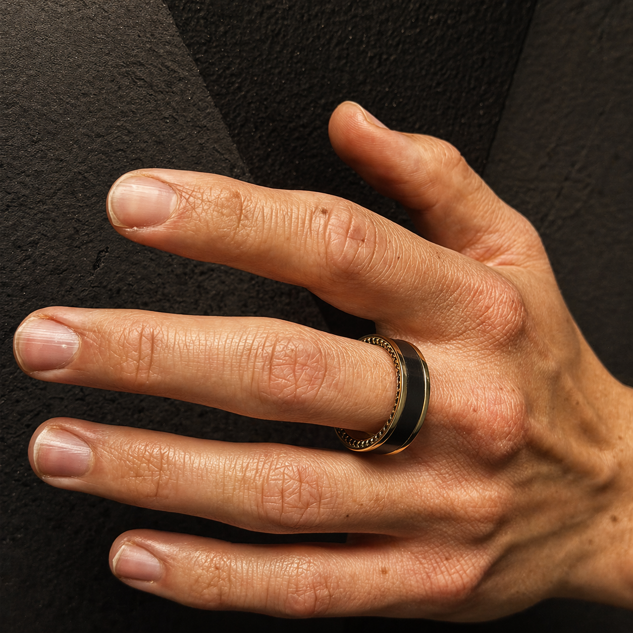 A close-up shot of a hand with a ring on the middle finger. The ring is a yellow gold reverse inlay design with a solid black diamond inlay and black diamonds on the inner edge.
