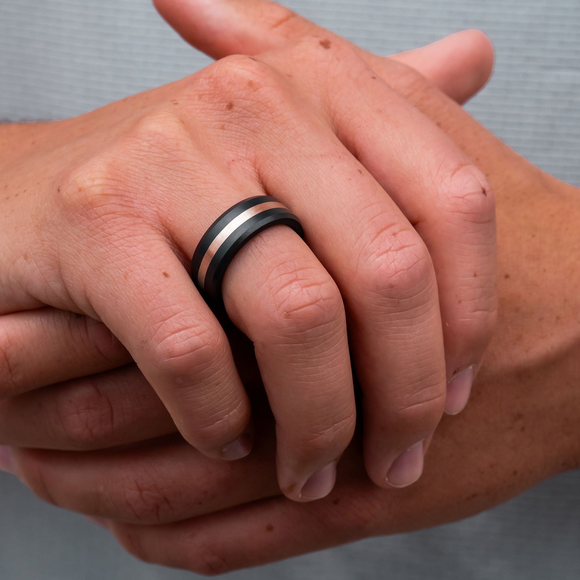 Lifestyle shot #2 of men's hands wearing our Elysium ARES Men's Black Diamond & 18k Rose Gold Inlay | ElysiumBlack.com | Men’s 18k Rose Gold Inlay Wedding Rings