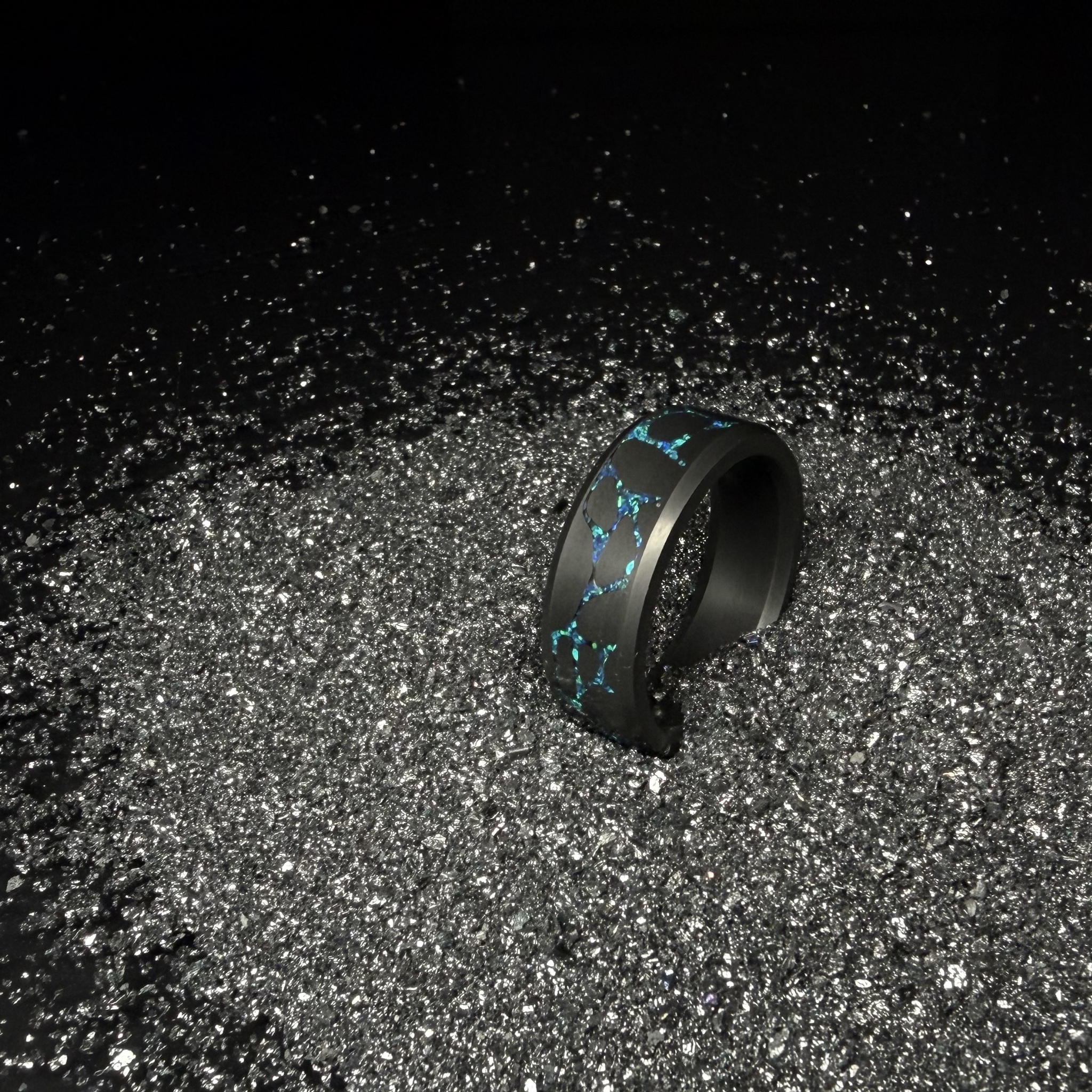 Solid Black Diamond ring with laser engraved river stone inlay filled with blue opal with silver dust in the background