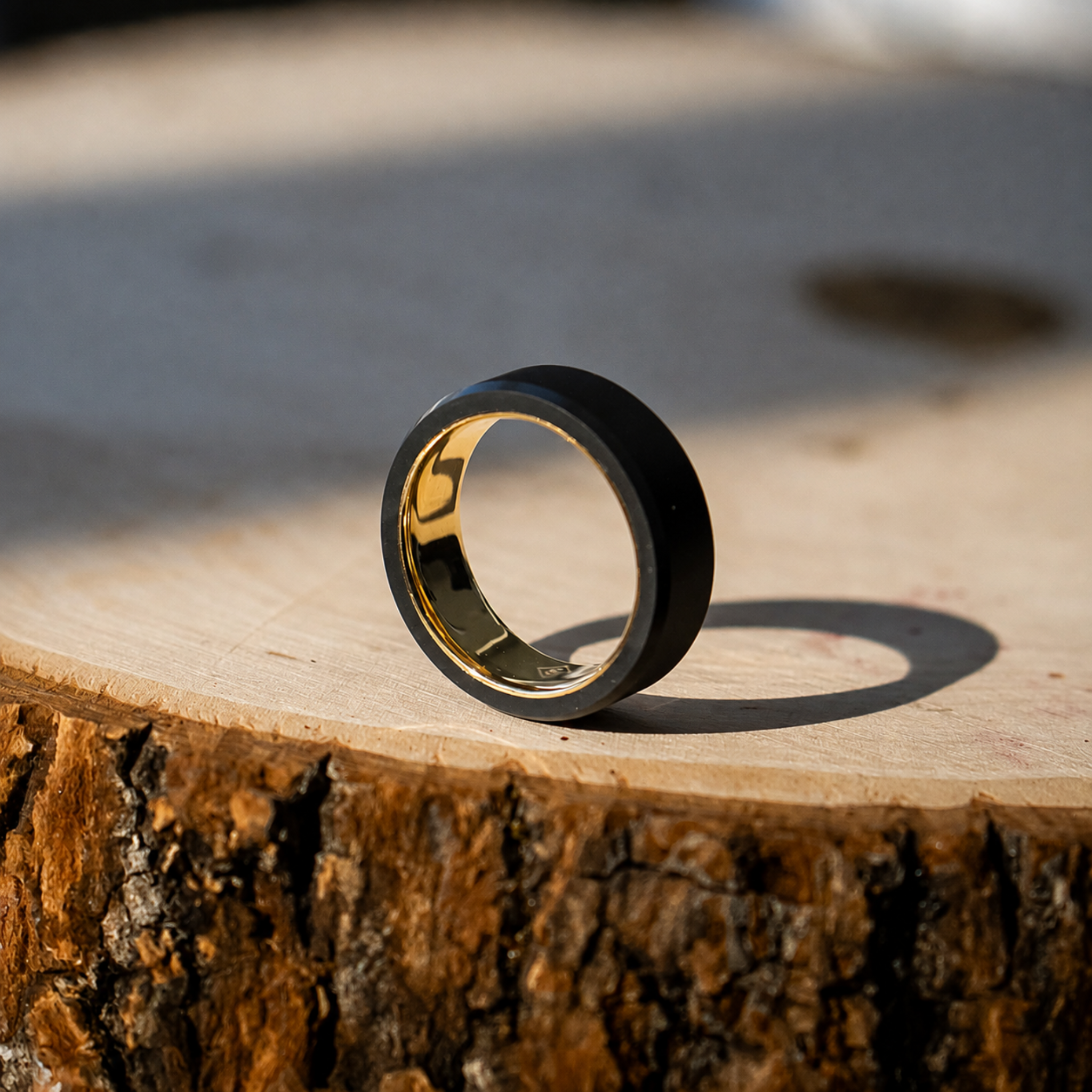 ARES 8mm solid black diamond wedding band with yellow gold interior, standing upright on a rustic wood log slice.