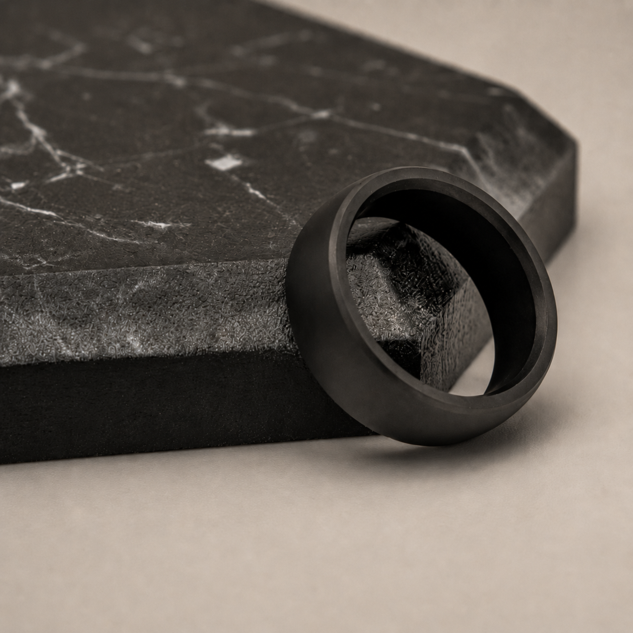 NYX 8mm solid black diamond wedding band resting on a dark gray marble slab against a warm beige background.